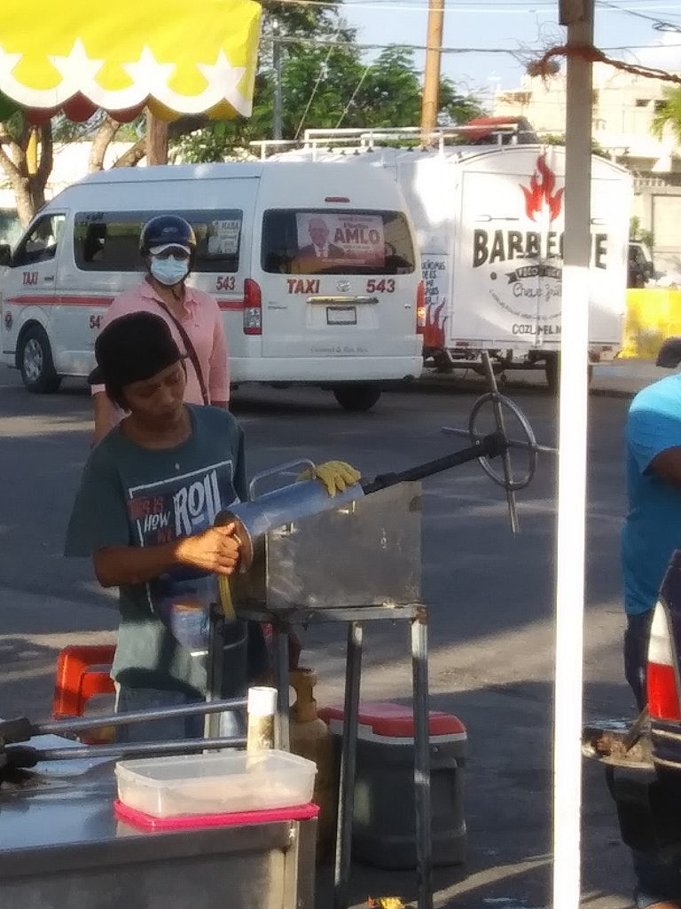 A youth in Cozumel Mexico at a churro street food booth. He is preparing the machine and pulling sections of extruded dough from it.