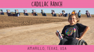 Girl in wheelchair holds a spray paint in front of Cadillac Ranch.