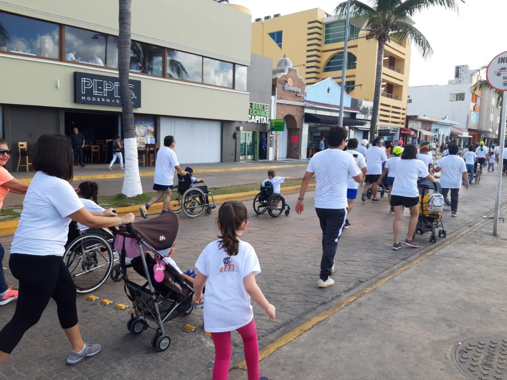 View from behind a group of paint runners as they make their way along the street route. Anna is visible in the middle of the screen rolling her wheelchair.