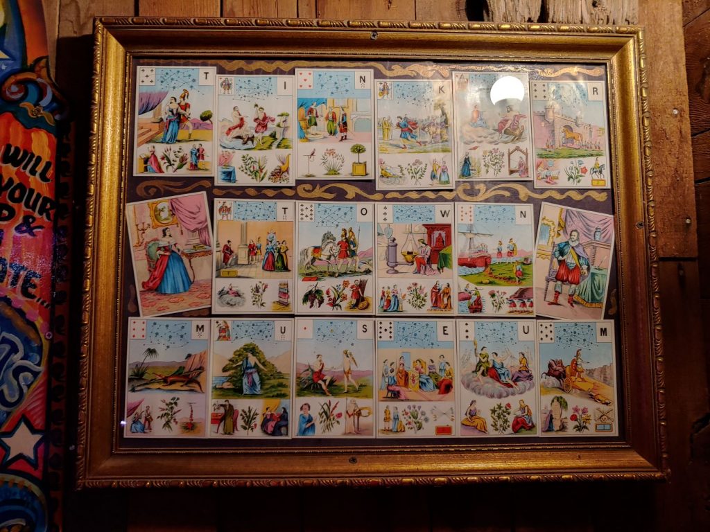 A framed collection of alphabet cards that are illustrated like children's literature. The frame is fancy embellished gold wood and hangs on a rough brown wood wall.