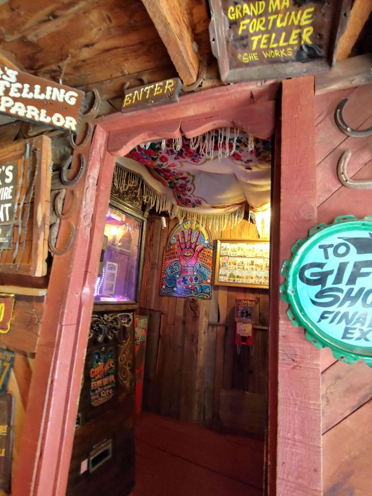 Doorway to a small closet-like room that holds the Fortune Teller machine. The doorway has a cardved upper piece with a sign above that reads Enter. There is fringe dangling from the edge of the ceiling inside the room.