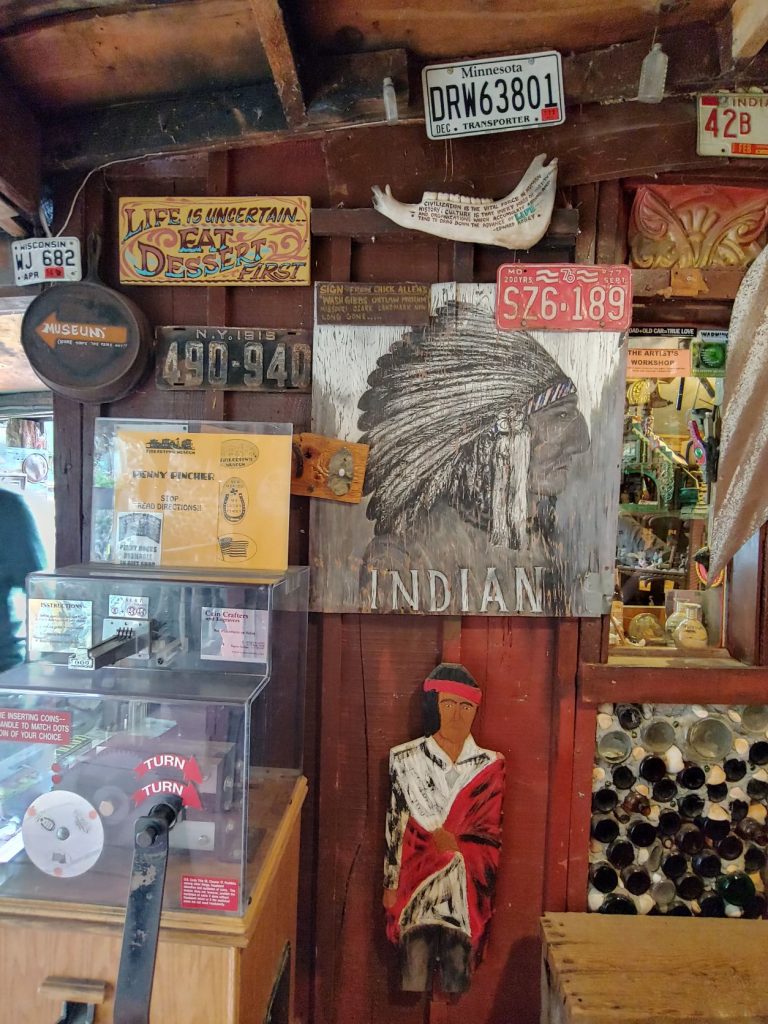 A purposefully cluttered wall in Tinker Town museum. Several old license plates and metal advertising signs on display.