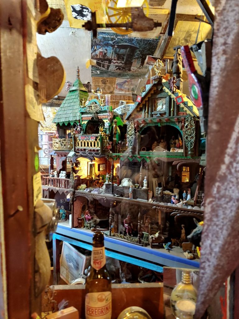 Handcarved village town scene with many intricate details and several buildings. Behind glass in a waist high display case built into a wall.