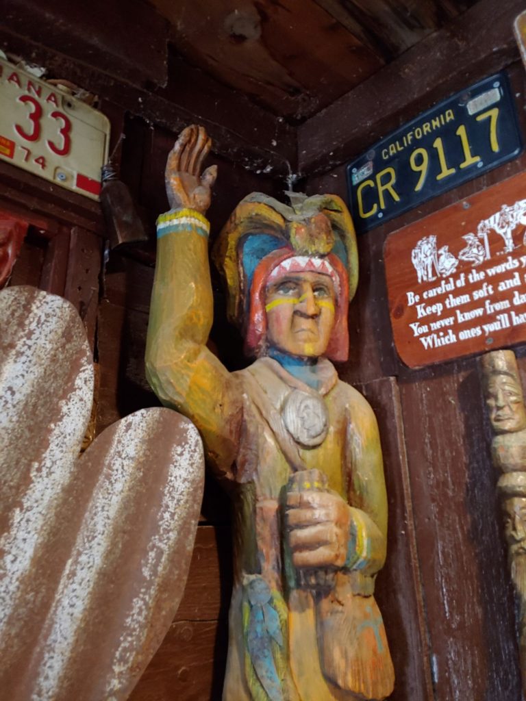A folk art style painted wood carved Cigar Store Indian. About 4 foot tall and standing on shelf in Tinker Town museum.