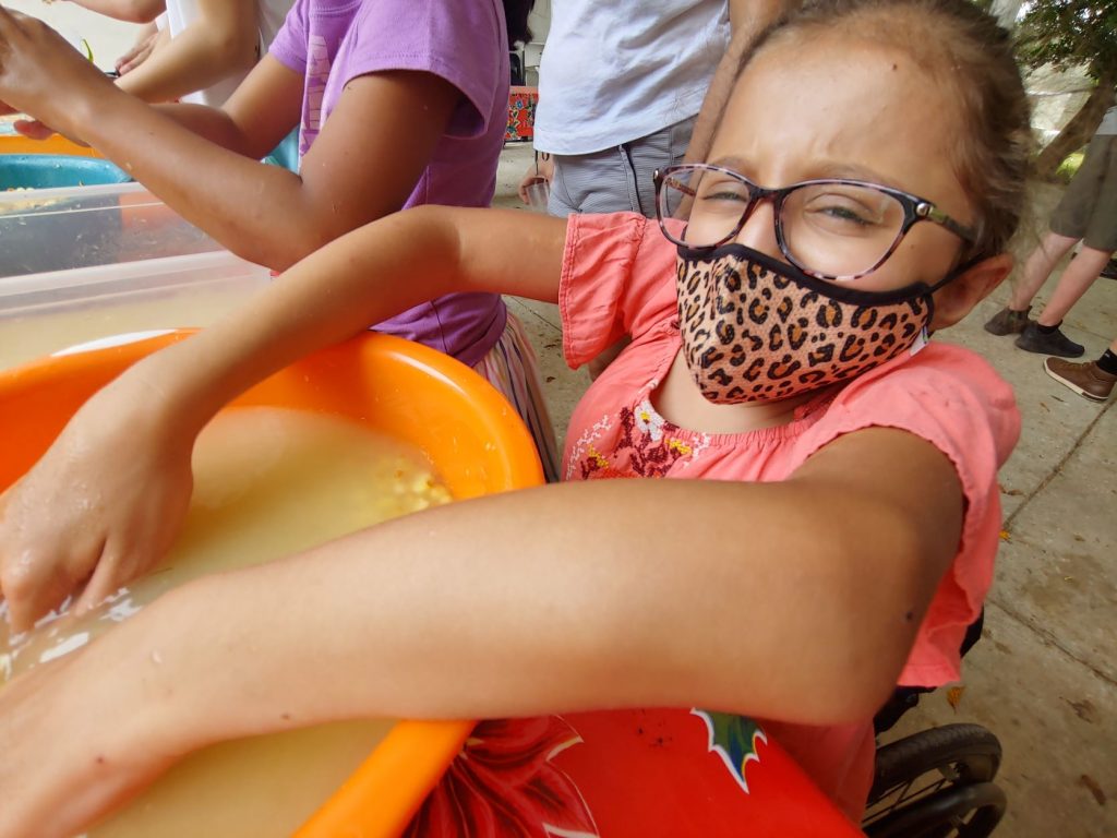 Teen girl in wheelchair washes corn as part of immersive cooking lesson while attending accessible Spanish lessons in Merida, Mexico.