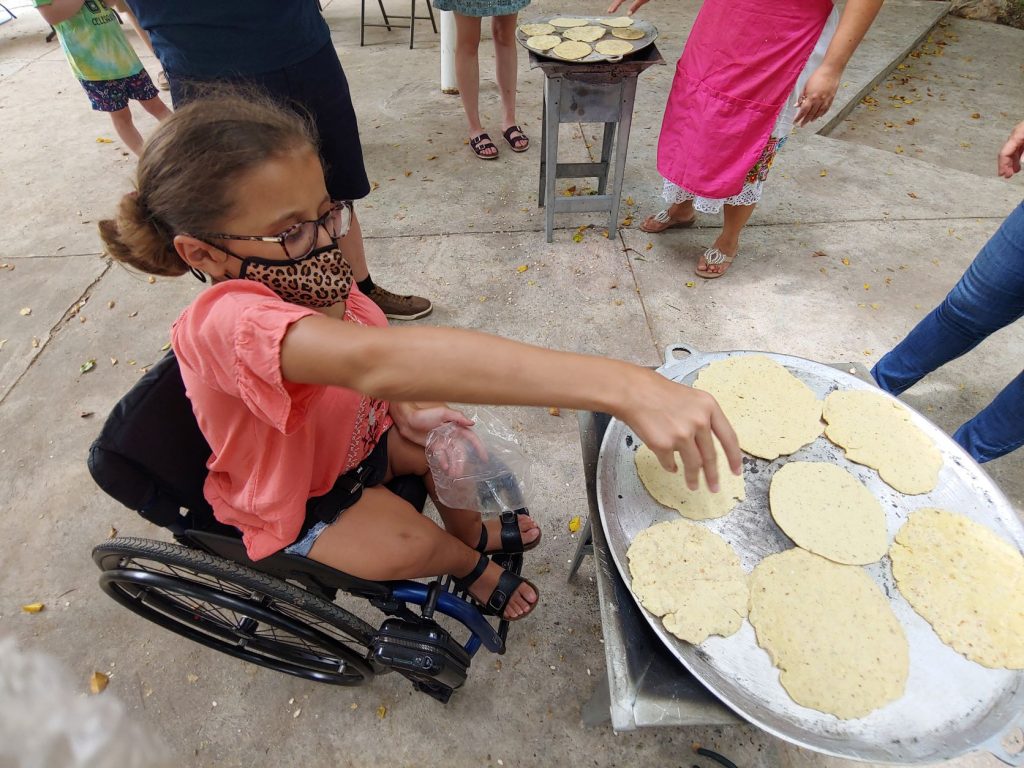 Girl in wheelchair learning to fry tortillas during accessible Spanish lesson in Merida, Mexico.