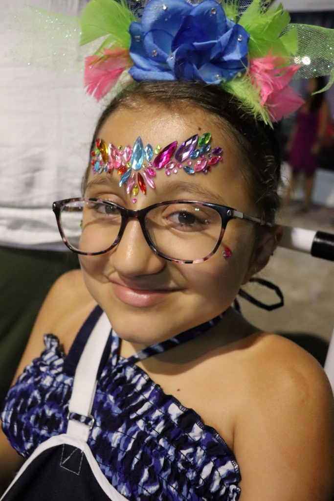 A teen girl wearing a blue dress with gems on her forhead sits in a wheelchair about to enjoy the parades of Cozumel's carnaval celebration showing the accessibility.