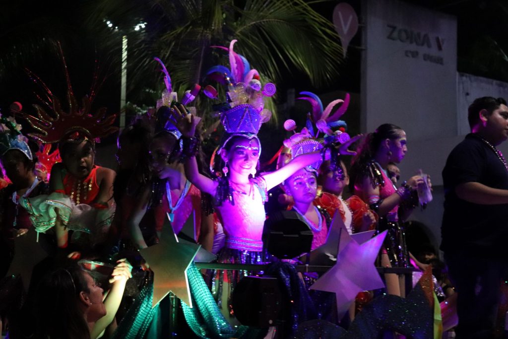 A young woman is lit in a purple light in the dark night as she rides a float in one of the Cozumel Carnaval parades.