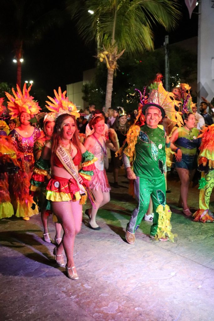 Three women in brightly colored yellow and red costumes walking in the Cozumel Carnaval parade with a middle aged man wearing a green costume.