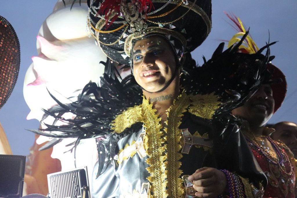 Male entertainer on a Cozumel Carnaval parade float wearing a silver satin with ornate gold trim long sleeve jacket and an oversized costume genie styled turban headpiece.