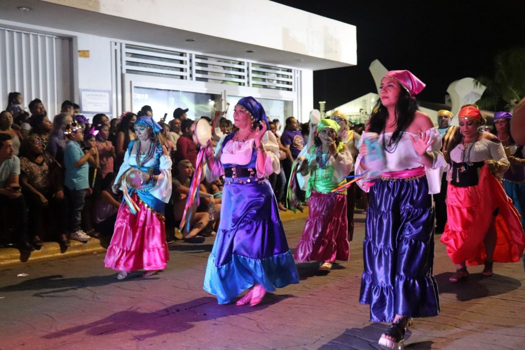 Women with colorful gypsy costumes with long flowy skirts and head scarves carrying tamborines walk in the Cozumel Carnaval parade.
