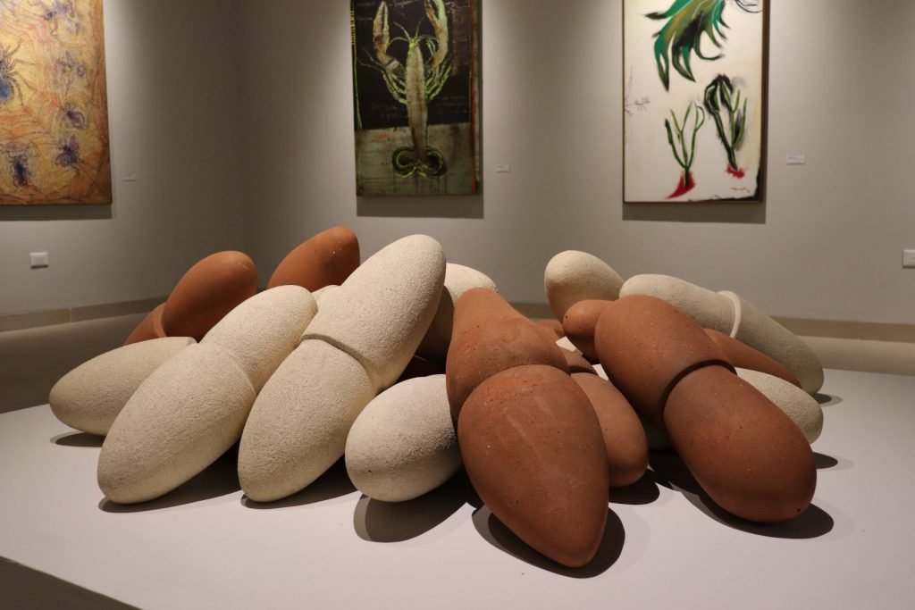 A large scale grouping of clay sculptural art pieces on a very low pedestal in the center of a room. There are several pieces of art on the walls surrounding it and they all have a nature theme with a lobster and seaweed depicted.