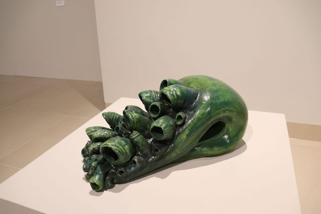 Large deep green sculpture on display in the gallery of Cozumel museum. It appears to have barnacles growing on it.