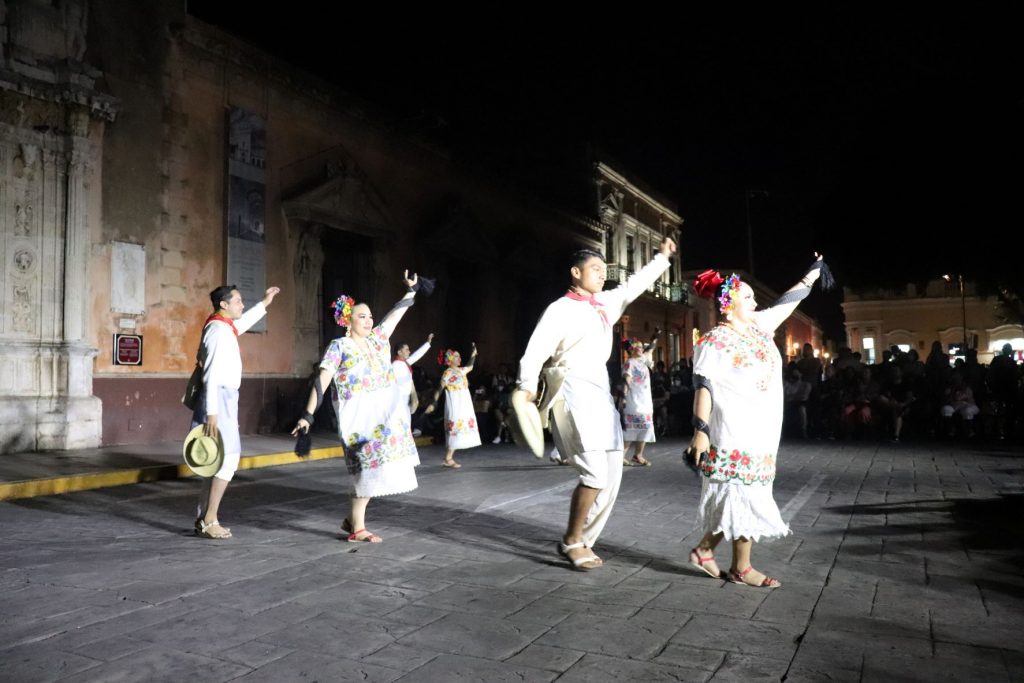 A few Latino dancers raise their left arms as they begin to take a step forward. One man wears a stern smile on his face, unlike the glowing smiles of many of the female dancers.