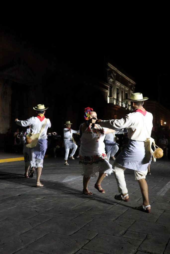 Pairs of Latino men and women dance jovially together on the stage. They hold hands and swing around in unison.