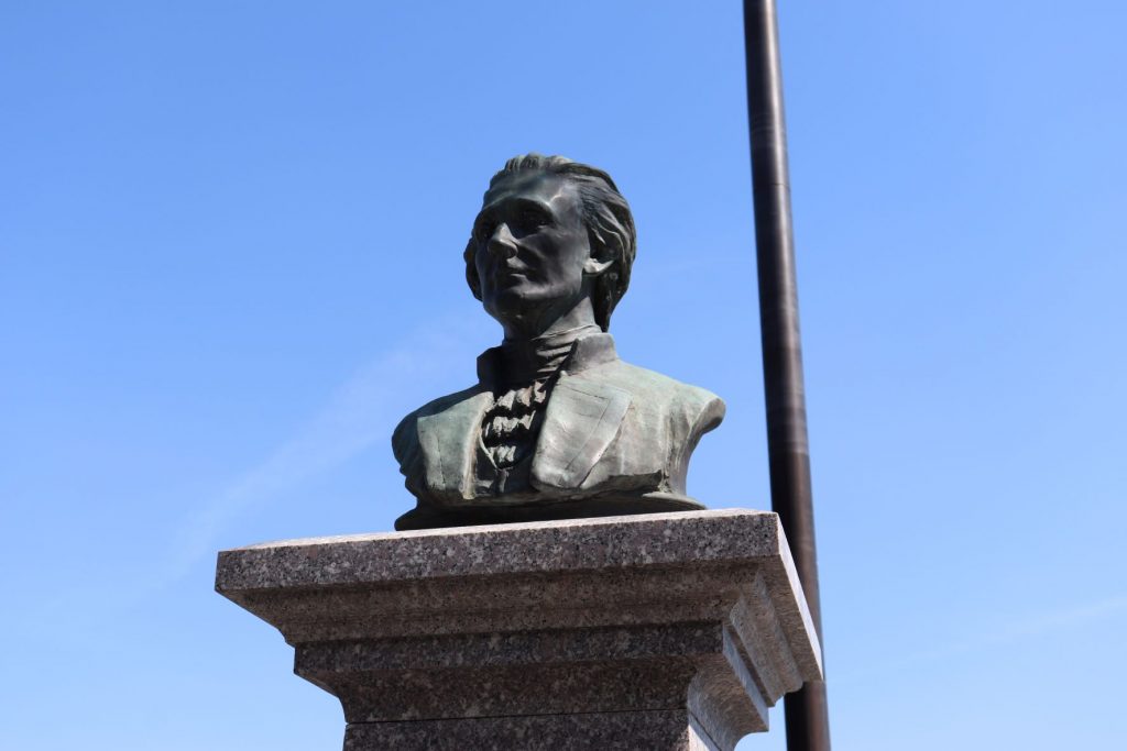 A close up of the Alexander Hamilton bust on the statue pedestal at Weehawkin Dueling Grounds. There is a beautiful clear blue sky filling the background.