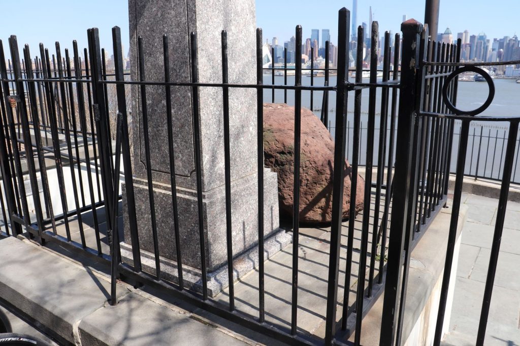 A close side view of the boulder directly behind the statue of Alexander Hamilton at the Weehawkin Dueling Grounds. This boulder is the one that Hamilton rested upon after he was shot. There is a black wrought iron fence surrounding this.