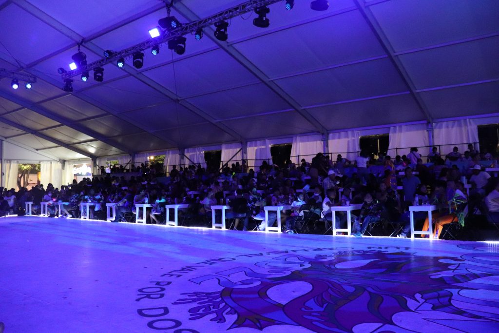 The floor of the Carnaval Palace with tables lining the edge and a large logo for the Cozumel Carnaval painted on the dance floor. The room is long and narrow with purple lighting overhead.