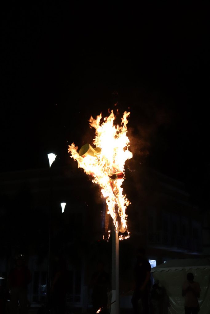 This close up shot of the Juan Carnival effigy in flames on the tall stand shows the contrast between the bright flames and the complete darkness surrounding.